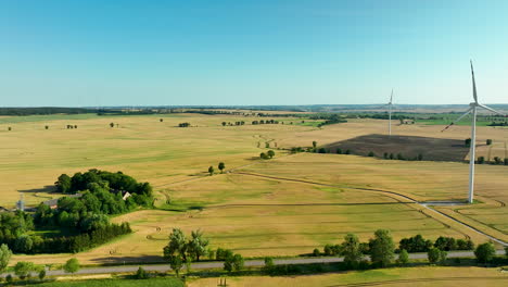 Aerial-shot-of-expansive-fields-with-wind-turbines-and-a-long-road-cutting-through-the-landscape,-showcasing-modern-agriculture-and-renewable-energy