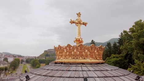 Cruz-Dorada-De-La-Cúpula-De-La-Basílica-Inferior-De-Lourdes-Con-El-Castillo-Al-Fondo.