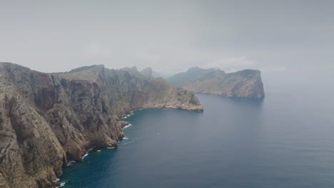 Aerial---steep-rugged-limestone-coastline-cliff-near-blue-water,-Mallorca