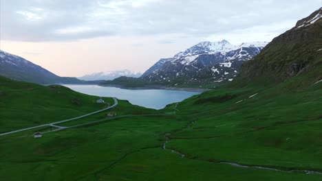 Vista-Aérea-Del-Lago-Mont-Cenis-Rodeado-De-Exuberantes-Campos-Verdes-Y-Montañas-Cubiertas-De-Nieve-Bajo-Un-Cielo-Nublado