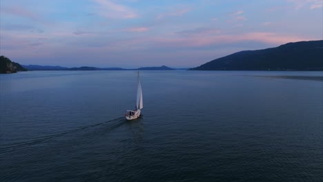 Niedrige-Luftumlaufbahn-Eines-Segelbootes,-Das-Bei-Sonnenuntergang-Auf-Dem-Ruhigen-Wasser-Des-Lago-Maggiore-Segelt