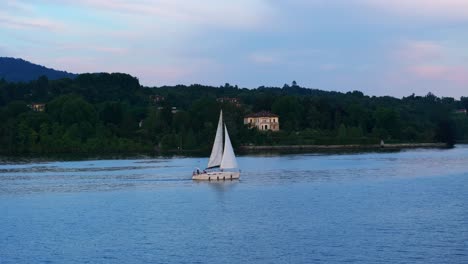 Vista-Lateral-De-Seguimiento-De-Un-Pequeño-Velero-En-El-Lago-Maggiore-Navegando-Al-Atardecer