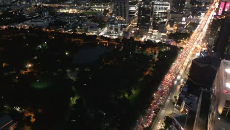 Aerial-drone-Fly-Bangkok's-Lumphini-Park,-business-commercial-district-at-night