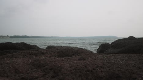 Vista-De-Un-Paisaje-Costero-Rocoso-Con-Piedras-Oscuras-Y-ásperas-En-Primer-Plano-Y-Aguas-Tranquilas-Del-Océano-Que-Se-Extienden-Hasta-El-Horizonte-Bajo-Un-Cielo-Nublado