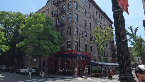 Some-white-people-walk-and-cycle-in-the-crossroads,-on-the-corner-of-Bedford-Street-and-Grove-Street-in-the-West-Village-neighborhood-of-Manhattan-of-at-the-famous-90-Bedford-Street,-New-York-City