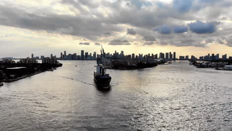 Drone-footage-of-a-cargo-vessel-entering-the-Port-of-Miami-from-the-Atlantic-Ocean,-showcasing-the-Miami-skyline-behind-it