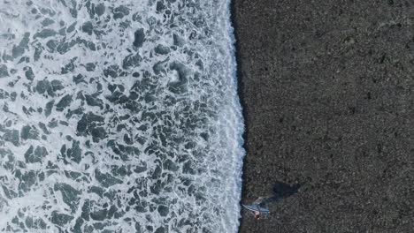 Von-Oben-Nach-Unten-Zeitlupen-Drohnenaufnahme-Der-Wellenbewegung-über-Einem-Korallenriff-Mit-Einem-Laufenden-Surfer-In-Uluwatu,-Bali,-Indonesien