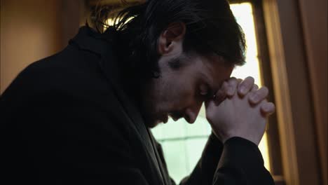 Young-man-in-old-church-building-in-front-of-stained-glass-window-kneeling,-praying,-worshipping