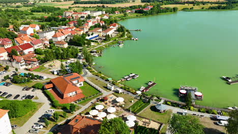 Aerial-view-of-the-lakeside-town-of-Ryn,-Warmia-Masuria,-showcasing-colorful-buildings,-a-marina,-and-the-green-waters-of-the-lake