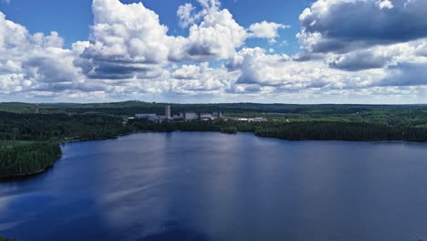 Garpenberg-mine-and-lush-greenery-by-a-serene-lake-under-a-cloudy-sky,-aerial-view,-hyperlapse