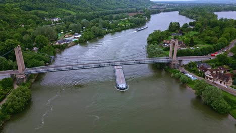 Barge-passing-under-suspended-bridge-on-Seine-River,-Les-Andelys,-France