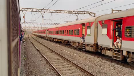 Indian-trains-run-parallel-as-commuters-thrill-in-standing-at-the-door,-feeling-the-rush