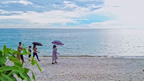 Asiaten-Spazieren-An-Einem-Heißen,-Sonnigen-Tag-Mit-Sonnenschirmen-An-Einem-Kiesstrand-Auf-Den-Philippinen-Entlang