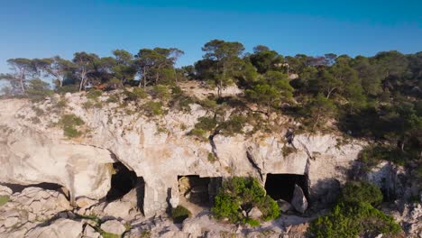 Flying-over-limestone-cliff-caves,-historic-heritage-near-beach,-Mallorca