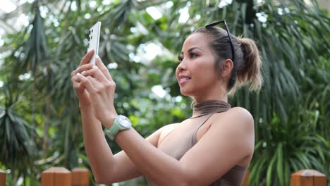 Mujer-Sosteniendo-Un-Teléfono-Inteligente-Y-Tomando-Una-Fotografía-De-La-Vegetación-En-Un-Jardín-Botánico