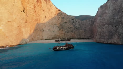 Revealing-aerial-footage-of-Navagio-Beach-with-a-cruise-ship-full-of-tourists-in-the-foreground