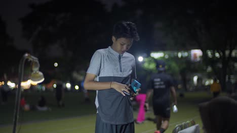 Young-Teenage-Boy-Pulls-Money-From-Smartphone-Casing-At-Ahmad-Yani-Square-At-Night-In-Tangerang,-Indonesia