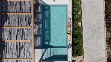 Brunette-woman-in-swimming-costume-lying-on-her-stomach-at-the-edge-of-a-pool-in-Cayo-Resort-in-Greece-Crete---she-basks-in-the-sun---drone-flies-down