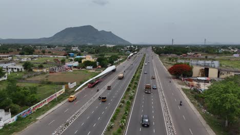 Toma-Aérea-De-Un-Dron-De-Una-Carretera-Con-Tráfico-Pasando-Con-Alas-De-Molino-De-Viento