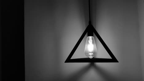 Close-up-black-and-white-triangle-lamp-making-light-and-shadow-on-the-wall,-static-shot-and-copy-space