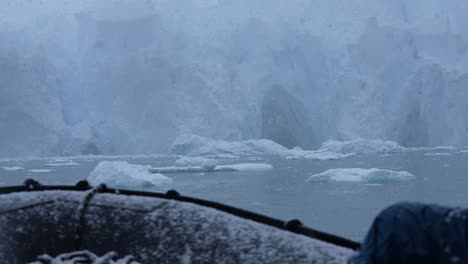 Antarctica-Expedition,-Rubber-Boat-Sailing-Under-Massive-Glacier-on-Snowy-Day,-Slow-Motion