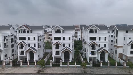 A-newly-constructed-row-of-identical-large-white-multi-story-villa-styled-houses-along-a-suburban-road