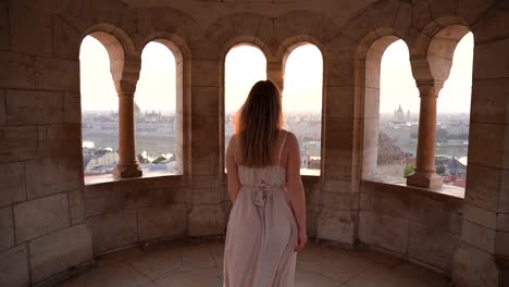 Young-woman-walking-in-Fisherman's-Bastion-in-a-dress-with-scenic-view-of-Budapest-and-Danube-on-a-sunny-day