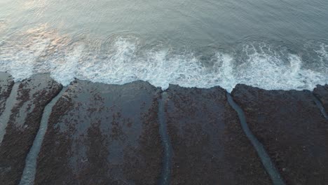 Slow-Drone-shot-of-Bingin-Beach-low-tide-reef-and-waves-at-sunset-in-Uluwatu-Bali-Indonesia