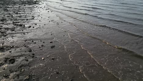 Arty-drone-shot-alone-the-river-Mersey,-seeing-the-waves-crash-along-the-beach