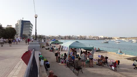 Maltesische-Familien-Machen-Ein-Picknick-Am-Strand-Unter-Zelten-Und-Die-Leute-Spazieren-Auf-Der-Promenade-An-Der-Hübschen-Bucht,-Birzebbuga,-Malta