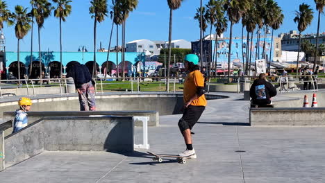 Algunos-Patinadores-Están-Entrenando-En-El-Skaterpark-Junto-A-La-Playa-Con-Palmeras-En-Un-Día-Cálido,-Cámara-Lenta-Y-Colores-Fuertes