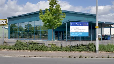 Vacant-car-dealership-lot-with-for-sale-sign-and-large-glass-facade,-Exeter,-Devon,-UK,-June-2024