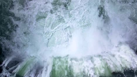 Top-down-aerial-drone-flight-overlooking-into-a-gushing,-extremely-powerful-waterfall-in-Iceland