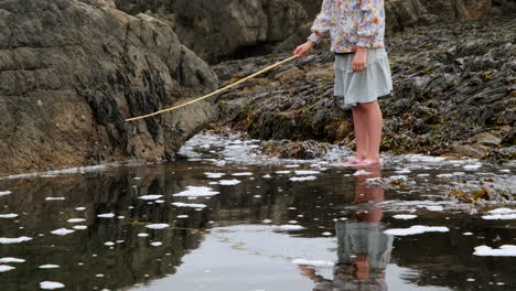 Niña-Pescando-En-La-Piscina-Del-Océano-En-La-Costa-Rocosa-Con-Su-Reflejo-En-El-Agua