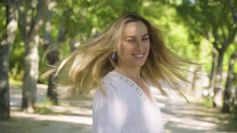 Cheerful-caucasian-young-blonde-woman-in-a-white-dress-is-walking-in-the-park