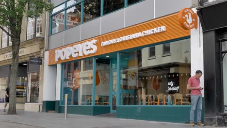 Exterior-facade-of-Popeyes-food-chain-store-with-customers,-Exeter-Devon-UK,-June-2024