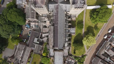 Top-down-drone-view-of-Exeter-Cathedral-as-major-restoration-work-is-underway,-surrounded-by-greenery-and-nearby-buildings