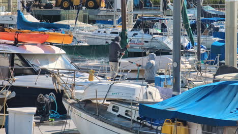 Cleaning-yatch-boat-in-the-marina-with-water,-scrubbing,-Los-Angeles-port,-USA