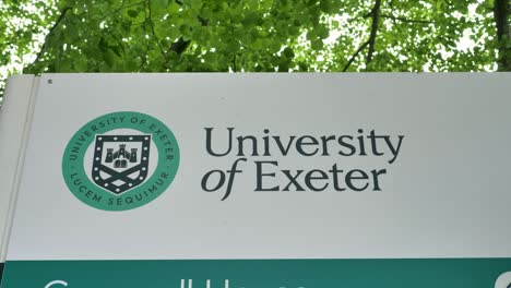 Logotipo-De-La-Universidad-De-Exeter-En-Un-Cartel-Con-árboles-En-El-Fondo,-Exeter,-Devon,-Reino-Unido,-Junio-De-2024