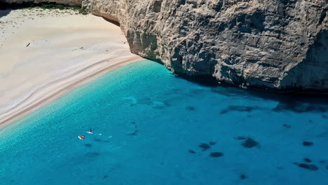 Navagio-beach-in-greece-with-a-paddleboarder-in-turquoise-waters,-aerial-view