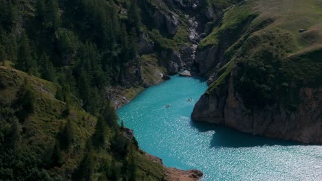 Aerial-view-of-kayakers-enjoying-the-serene-turquoise-waters-of-Mont-Cenis-Lake,-surrounded-by-lush-greenery-and-rocky-cliffs