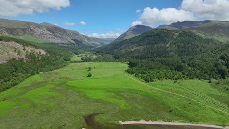 Wide-green-valley,-lake-shore,-forested-hillsides-and-mountains