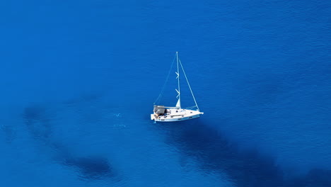 A-lonely-sailboat-in-the-middle-of-the-Blue-Ocean,-slow-aerial-panoramic-shot