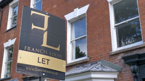 Let-estate-agent-sign-outside-of-red-brick-house-windows-with-greenery,-Exeter,-Devon,-UK,-June-2024