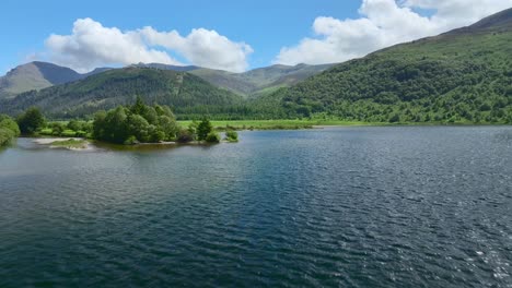 Flying-over-lake-towards-forested-hillsides-with-rise-revealing-flat-grassland