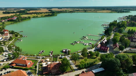 Aerial-shot-of-the-picturesque-town-of-Ryn,-Poland,-featuring-a-serene-lake,-residential-areas,-and-lush-green-surroundings