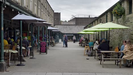 Public-enjoying-the-bustling-Pannier-market-in-Tavistock,-Devon,-UK,-engaging-with-local-vendors-and-community-activities,-June-2024