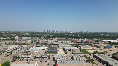 Drone-rising-to-reveal-Winnipeg-skyline-under-clear-blue-sky,-stores-and-houses-in-foreground