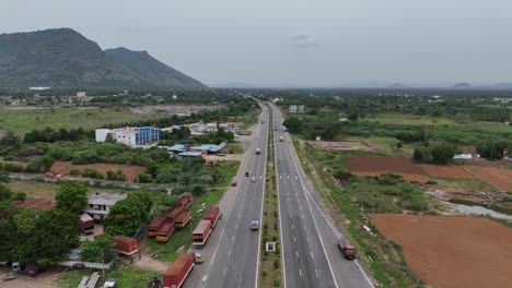 Elevated-footage-of-the-highway-passing-through-a-vibrant,-bustling-town-with-Mountain-in-background