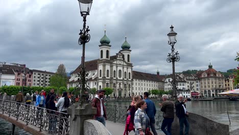 Tourist-on-bridge-crossing-river-with-famous-Jesuit-Church-of-Lucerne-Town-in-background